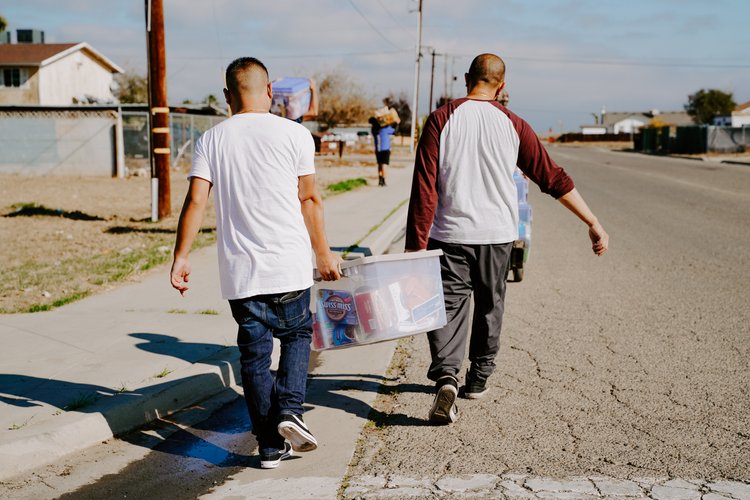 Two men carrying a bin of food